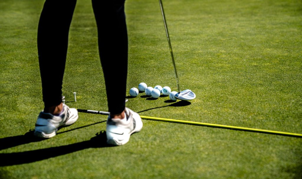 A golfer practicing putting on a sunny day with several golf balls on the green.